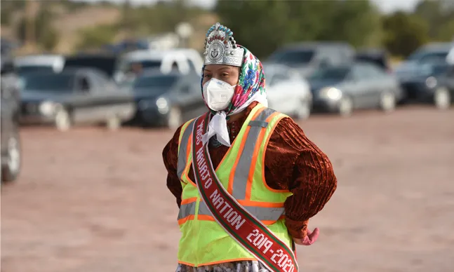 A person of Native American heritage with a small headdress wearing a reflective jacket and directing traffic